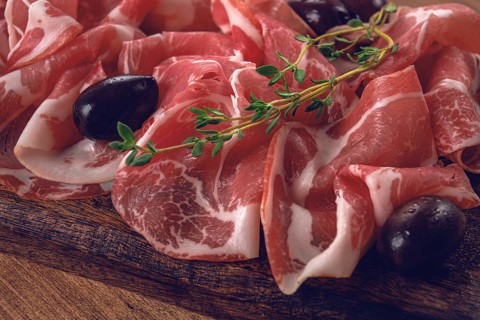 Freshly cut dried meat, served with olives and herbs, on a wooden chopping board, no people