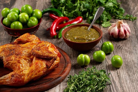 Baked tobacco chicken, served with tkemali sauce, on a wooden table, Georgian cuisine, rustic