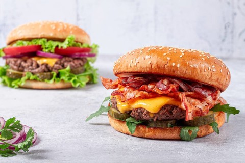 Two burgers with beef patty, fried bacon, cheddar cheese, tomatoes, homemade, no people