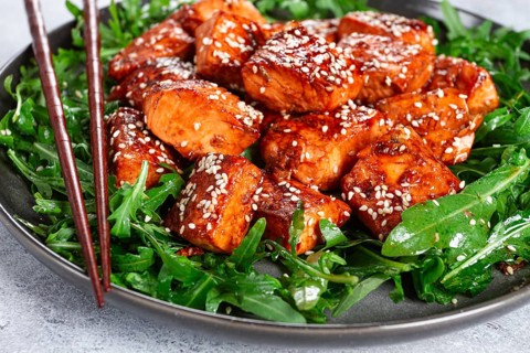 Fried salmon slices, teriyaki with sesame seeds, with arugula salad, top view