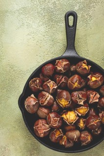 Roasted chestnuts, in an iron pan, wooden table, top view, no people, rustic style