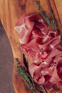Slices of cured meat neatly arranged on a wooden board with fresh herbs in a rustic kitchen setting