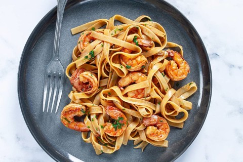 Fettuccine pasta with shrimp, spicy in soy sauce, on a grey plate with a fork, close-up