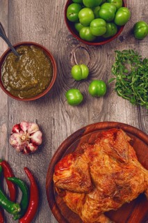 Baked tobacco chicken, served with tkemali sauce, on a wooden table, Georgian cuisine, rustic