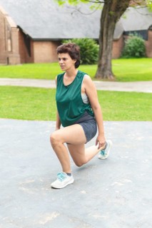 A focused woman performing a lunging stretch in a public park