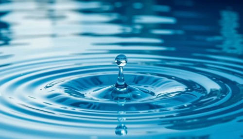 A close-up shot of a water droplet falling into a calm body of water, creating ripples that expand