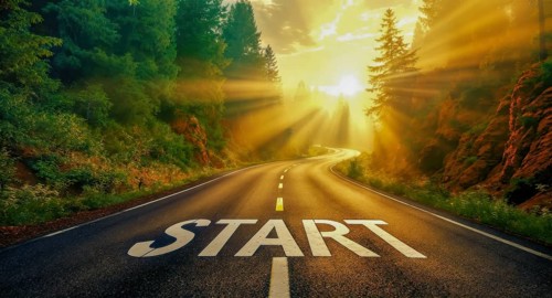 An open road with the word 'start' painted on it, illuminated by sunlight and surrounded by green