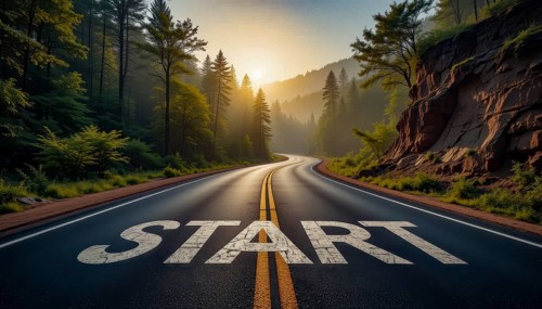 A winding road through a lush forest at sunrise, the word 'START' painted on the pavement,