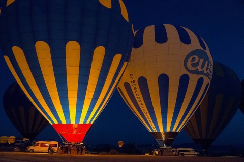 Illuminated hot air balloons glow in the dark, surrounded by a tranquil landscape, Göreme National