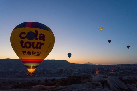 A balloon floats calmly at sunrise with the silhouetted landscape in the background, Göreme