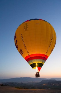 A large, luminous balloon floats over a clear mountainous landscape at dawn, Göreme National Park,