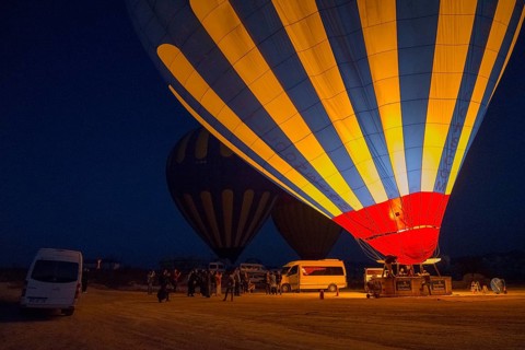Hot air balloons at night with people and vehicles, bright colours in contrast to the dark sky,