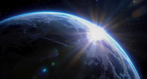 The sun rises over earth, illuminating the planet from space with a bright glow, surrounded by