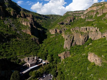 Gorge with lush greenery and rocks under a blue sky with clouds, aerial view, Geghard Monastery,