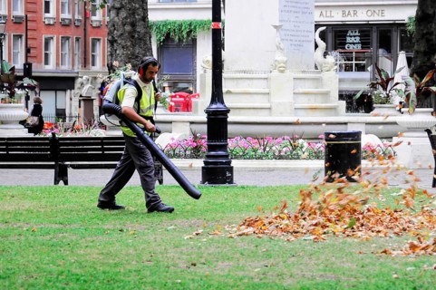A worker uses a leaf blower to remove leaves in a municipal park, London, England, United Kingdom