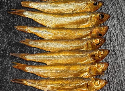 Arrangement with lots of fresh smoked sprats on dark stone slab