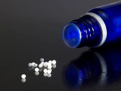 Detail of a open small blue bottle on dark reflective ground with globules around