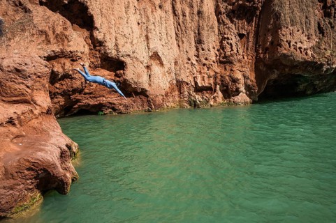A Moroccan woman in swimsuit jumps headfirst into the water under a waterfall Ouzoud in Morocco