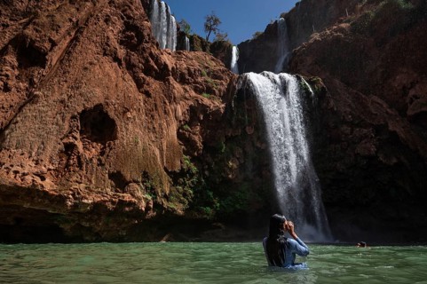 A Moroccan woman in swimsuit swimms under a waterfall Ouzoud in Morocco