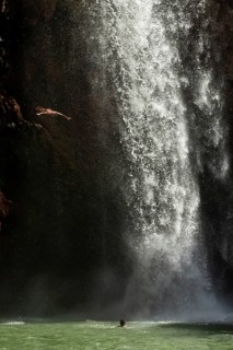 Moroccan young man jumps from the high rock into the water under a waterfall Ouzoud