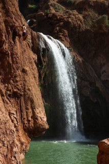 A Moroccan young man jumps from the high rock into the water under a waterfall Ouzoud