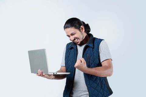 Male celebrating with fist in the air holding a laptop on white background. Young man celebrating