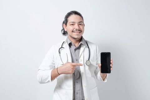Smiling young doctor pointing at the phone