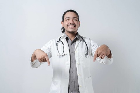 Smiling doctor pointing down isolated. Young latin doctor pointing down isolated