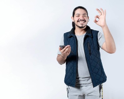 Smiling man gesturing approval with his phone in hand. Young man gesturing approval on the