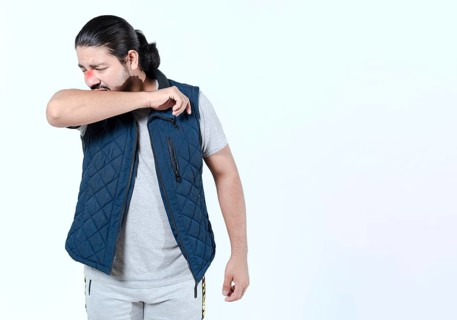 Young man sneezing into his arm isolated. Person with allergies sneezing on his arm