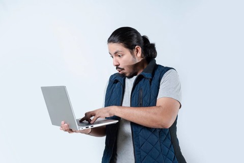 Man surprised looking at the computer he is holding on isolated