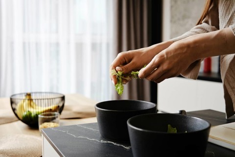 Hands gently tear lettuce leaves while preparing a fresh salad. The kitchen features contemporary