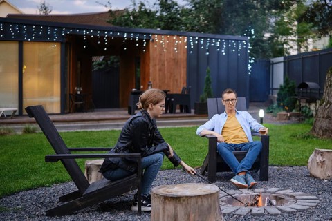 Father and his daughter sit by a fire pit in a backyard, engaging in conversation as the sun sets.