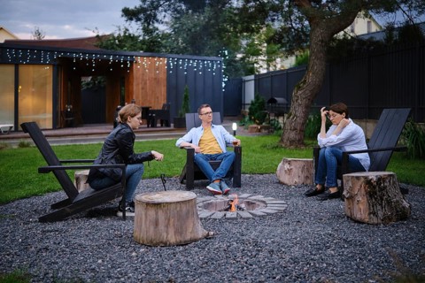 A family gather around a small fire pit in a backyard of tiny house, enjoying each their company.