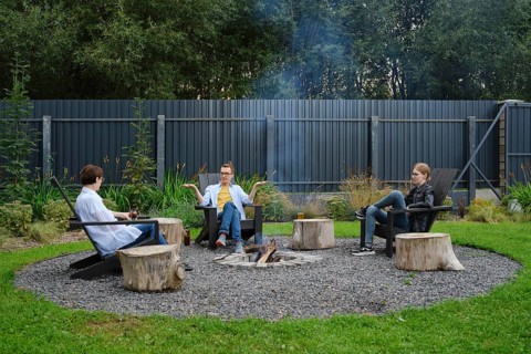 A family enjoy a relaxing evening around a fire pit in a backyard. They are sitting on wooden