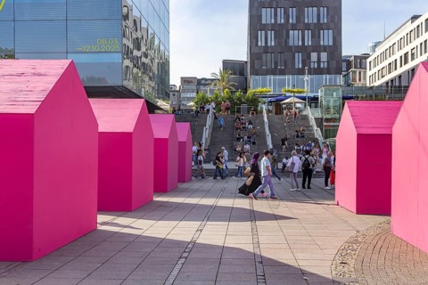 Twelve houses in bright magenta stand on Stuttgart's Schlossplatz in front of the art museum. The