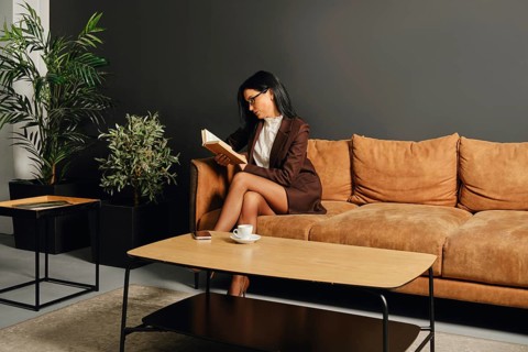 A woman dressed in a smart outfit is enjoying a quiet moment with a book on a cozy couch. The