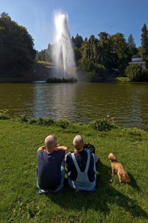 Couple with dog at the water games at the big pond with the high rising fountain, Bergpark