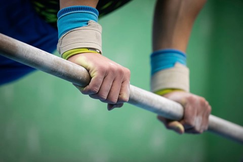 Close up of a gymnastics athlete gripping a sports bar with white chalk on their hands, AI