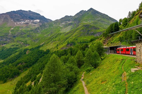 Beautiful Passenger Train Bernina Express on Mountain Alp Grüm in Swiss Alps in a Sunny Cloudy