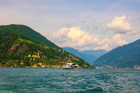 Passenger Ship on Lake Lugano and House and Church on Mountain Range in a Sunny Summer Day on the