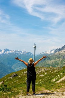 Woman with Arms Outstretched Standing in Front of a Wind Turbine with Mountain in the Swiss Alps