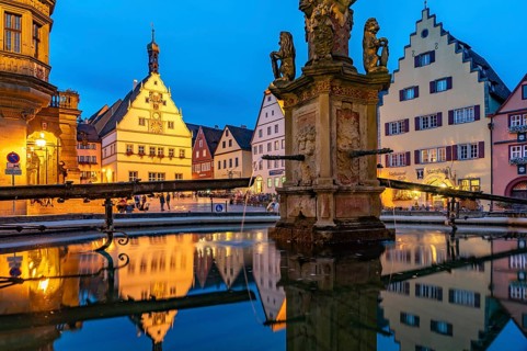 The market square with the Ratstrinkstube is reflected in the Georgsbrunnen fountain at dusk,