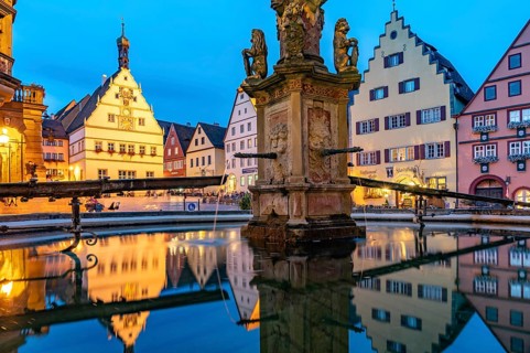 The market square with the Ratstrinkstube is reflected in the Georgsbrunnen fountain at dusk,