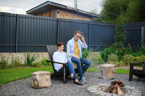 Two people enjoy a tranquil moment by the fire pit in a lush backyard. They share stories and