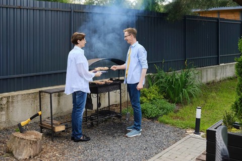 Wife assist her husband to grill meat skewers in a backyard/ They enjoying a sunny afternoon.