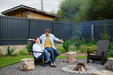 A couple spends a relaxed evening outdoors near a fire pit in their backyard. They share playful