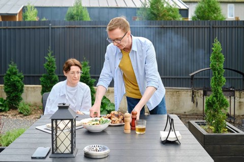 In a charming garden, a man serves a freshly prepared meal to a woman seated at a table