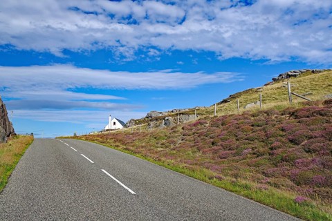 Lonely road through hilly landscape with a white cottage in the background, Isle of Lewis Hebrides,