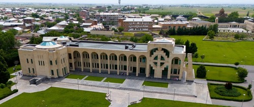 A modern building with geometric patterns surrounded by green spaces and streets, aerial view,